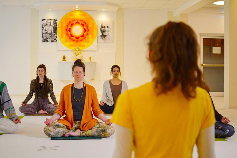 Meditation Ausbildung bei Yoga Vidya Meditationsgruppe sitzt im Seminarraum, angeleitet von einer Person im Vordergrund