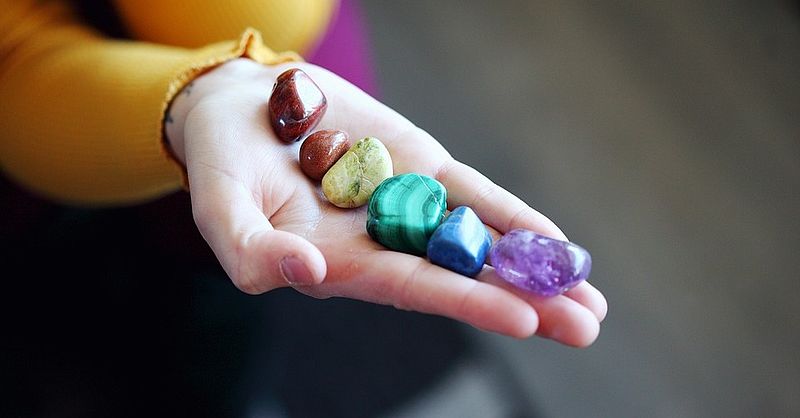 Hand mit 7 Chakra- symbolisierenden Edelsteinen