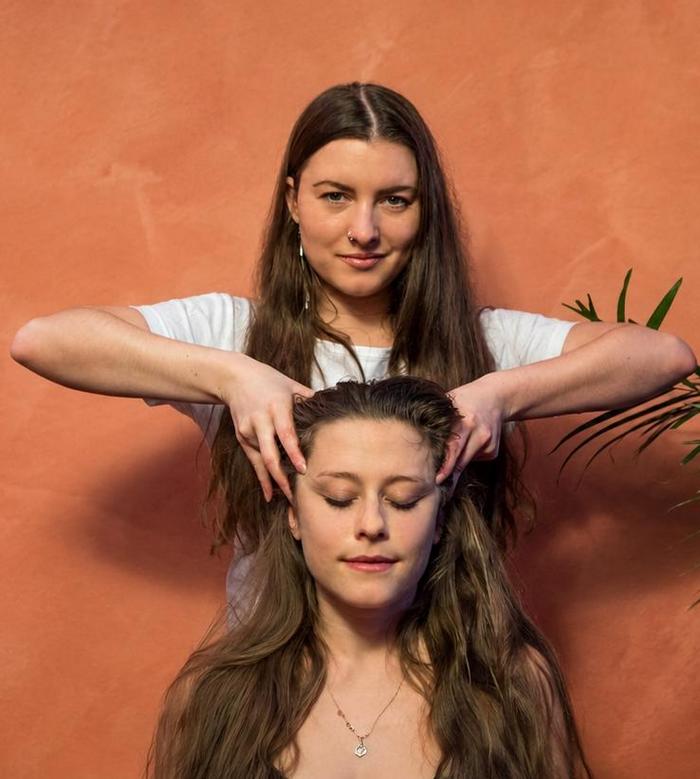 Frau erhält im Sitzen eine Kopfmassage und hält die Augen geschlossen