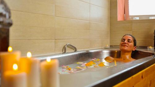 Frau entspannt in einer Badewanne mit Blütenblättern bei Kerzenlicht