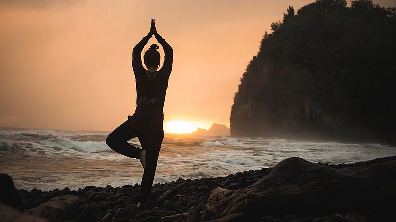 Frau am Strand praktiziert Yoga im Sonnenuntergang