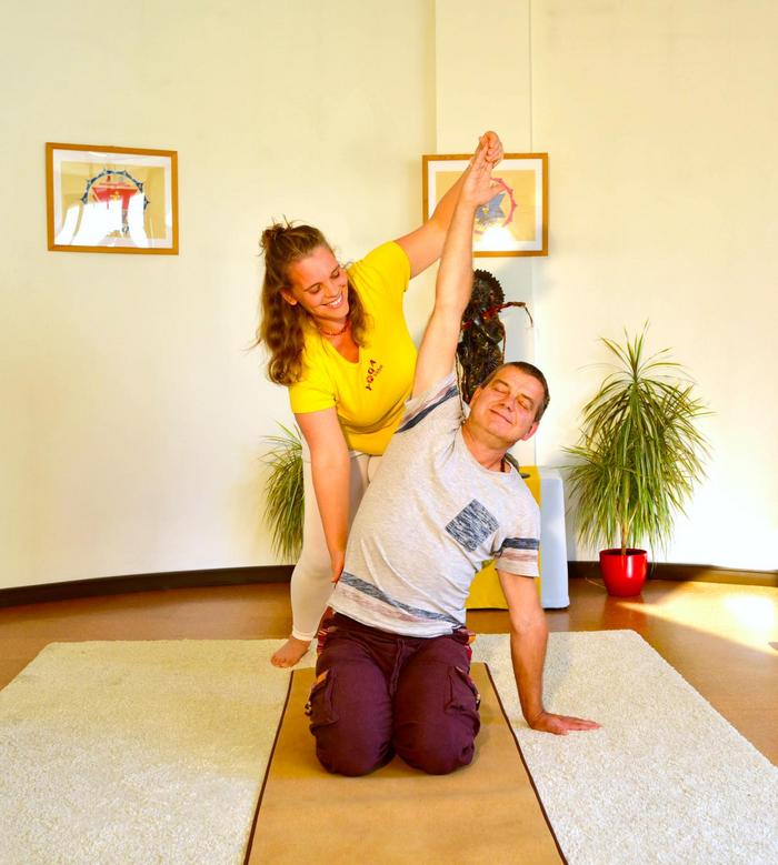 Ein Mann wird bei einer Yoga-Seitbeuge im Knien individuell unterstützt