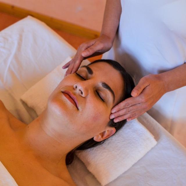 Ayurveda bei Yoga Vidya – Wissen und Anwendungen Frau liegt mit geschlossenen Augen auf einer Behandlungsliege und erhält eine Gesichtsmassage