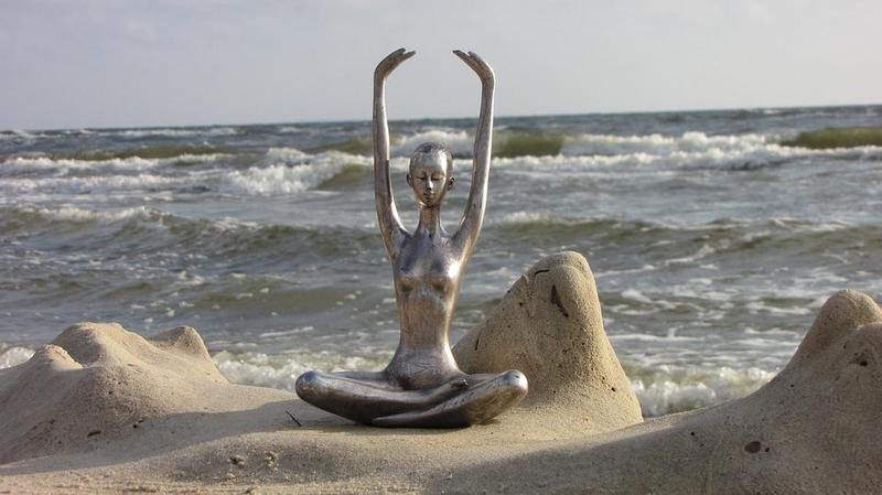 Silberne Statur in meditativer Pose an der See