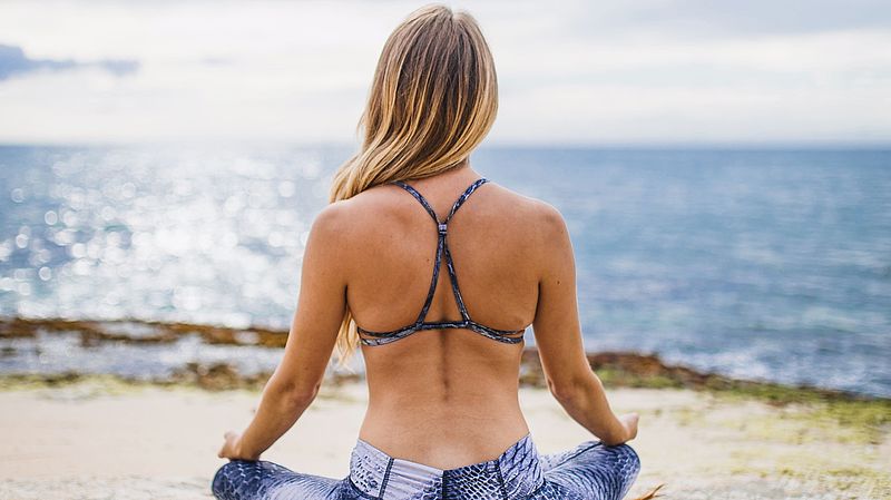Junge Frau in Yogakleidung an der See meditierend